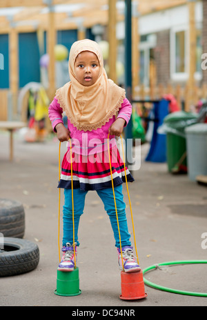 Der St.-Pauls-Kindergarten und das Kinderhaus, Bristol UK - A somalische Mädchen auf Stelzen auf dem Spielplatz spielen. Stockfoto