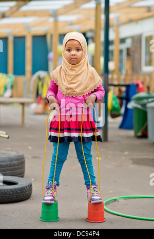 Der St.-Pauls-Kindergarten und das Kinderhaus, Bristol UK - A somalische Mädchen auf Stelzen auf dem Spielplatz spielen. Stockfoto