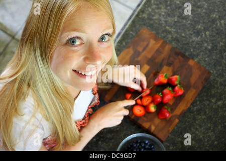 Eine attraktive Frau sucht in die Kamera Lächeln, wie sie Erdbeeren zerschneidet. Stockfoto
