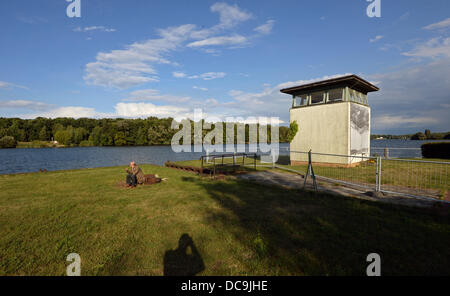 Potsdam, Deutschland. 13. August 2013. Ein Mann sitzt neben einem Turm der ehemaligen DDR Checkpoint an der Grenze entlang der Route der Berliner Mauer zum 52. Jahrestag des Baus der Berliner Mauer im Jahr 1961 steht vor einer übergroßen Foto in Potsdam, Deutschland, 13. August 2013. Foto: RALF HIRSCHBERGER/Dpa/Alamy Live News Stockfoto