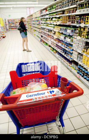 Eine Frau einkaufen von Lebensmitteln in Carrefour Supermarkt, Französisch mit ihrem Wagen in den Gang, der Dordogne, Frankreich Europa Stockfoto