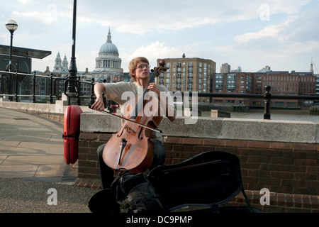 Ein junger Mann Straßenmusiker spielen klassische Musik auf dem Cello mit Blick auf St. Pauls Kathedrale Southbank London KATHY DEWITT Stockfoto