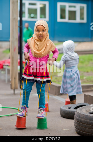 Der St.-Pauls-Kindergarten und das Kinderhaus, Bristol UK - A somalische Mädchen auf Stelzen auf dem Spielplatz spielen. Stockfoto