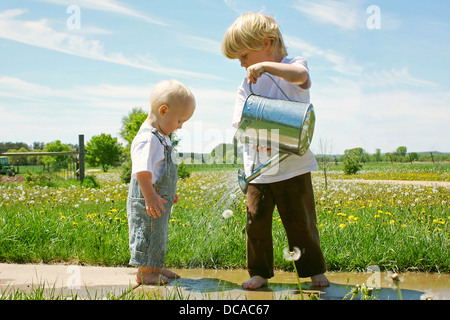 Ein kleines Kind wässert die Füße seines Bruders Baby an einem sonnigen Frühlingstag. Stockfoto