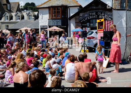 Erwachsene und Kinder beobachten ein traditionelles Kasperletheater am Meer in Looe. Stockfoto