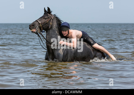 Bademeister Schwimmen mit Pferd im Meer am Holkham Beach in North Norfolk während ihrer jährlichen Sommerlager Stockfoto