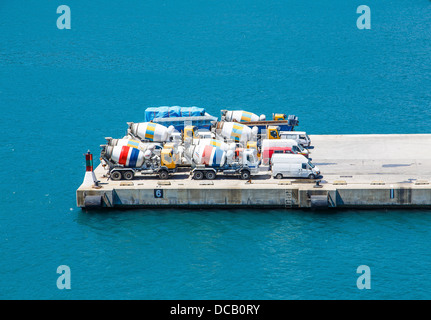 Reihen von bunten Betonmischer LKW geparkt auf einem konkreten Pier über dem blauen Wasser Stockfoto