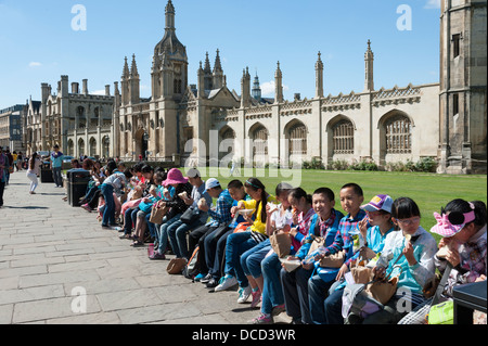 Junge chinesische Kinder Touristen aufgereiht an der Wand außerhalb des Königs College Cambridge UK Mittagessen oder Picknick Stockfoto