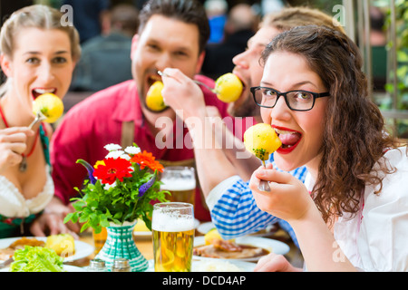 Junge Menschen in traditionellen bayerischen Tracht Verzehr von Schweinefleisch in Restaurant oder Pub zum Mittag- oder Abendessen Stockfoto