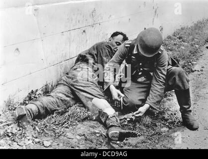 Ein Mitglied des Ärztekorps (Rod of Asclepius auf der Uniform) der deutschen Wehrmacht leistet während der sogenannten Operation Jubilee (Dieppe RAID) in Dieppe, Frankreich, im Sommer 1942 erste Hilfe. Fotoarchiv für Zeitgeschichte Stockfoto