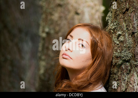 Ein horizontales Bild einer schönen jungen Frau, die an einen Baum gelehnt Stockfoto