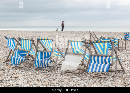 Liegestühle bei starkem Wind auf einen Kieselstrand mit einer Frau, Blick auf das Meer, Bier in Devon. Stockfoto