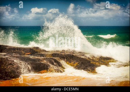 USA, Kauai, Hawaii. Eine Welle bricht auf den Felsen am Kauapea Strand, im Volksmund bekannt als Secret Beach. Stockfoto