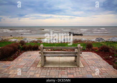 Eine Bank mit Blick auf den Lake Michigan Surf an einem kalten und regnerischen Frühlingstag Wind Zeitpunkt, Racine, Wisconsin, USA Stockfoto