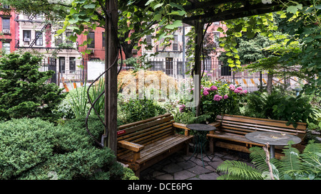 eine Laube mit Sitzgelegenheiten bietet einen ruhigen Ort zum Entspannen inmitten von viel Grün & Blumen in West 48th Street Community Garten New York Stockfoto