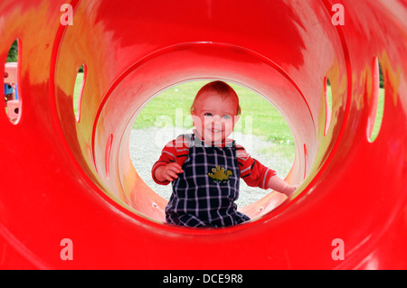 Ein lächelndes baby boy (im Alter von 16 Monaten) in einem rotem Kunststoff Rohr in einen Spielplatz Stockfoto