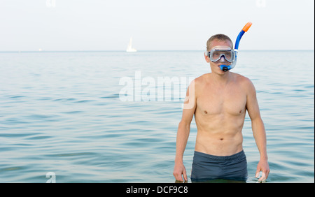 Junger Mann trug einen Schnorchel und Brille stehen in einem ruhigen Meer, als er bereitet Fähnrich zu gehen und die marine Unterwasserwelt zu erkunden. Stockfoto