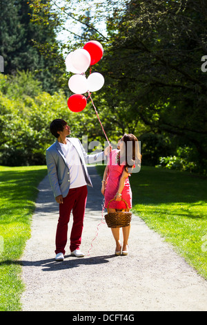 Vertikale Foto jungen Erwachsenen Paares dressed in formelle Kleidung betrachten mehrere Ballons halten Sie Picknick-Korb mit walki Stockfoto