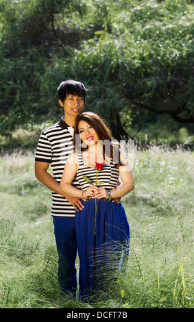 Vertikale Foto jungen Erwachsenen Paares halten einander, mit einzelnen roten Rose in der Hand der Frau, in der Wiese Stockfoto