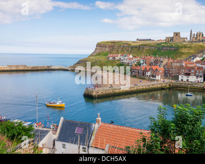 Ein Ausflugsschiff in Whitby Hafen mit Hütten auf der Ostseite der Stadt und Str. Marys Kirche im Sommer Stockfoto