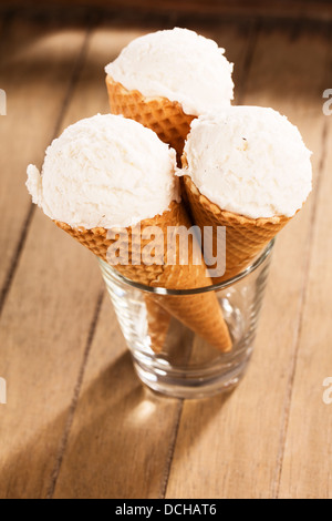 drei Vanilleeis Kugeln in Waffelkegeln stehend in einem Glas auf hölzernen Hintergrund Stockfoto