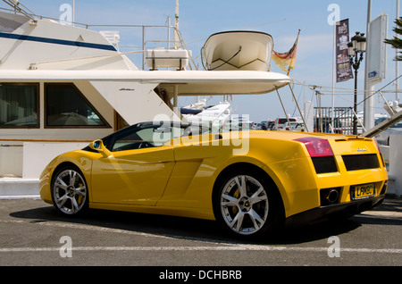 Einem gelben Lamborghini Gallardo Cabrio geparkt vor eine Luxus-Yacht in den Hafen von Puerto Banus, Marbella, Spanien. Stockfoto