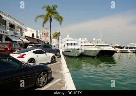 Sport Autos geparkt neben Yachten in der Luxus-Yachthafen von Puerto Banus, Marbella, Spanien. Stockfoto