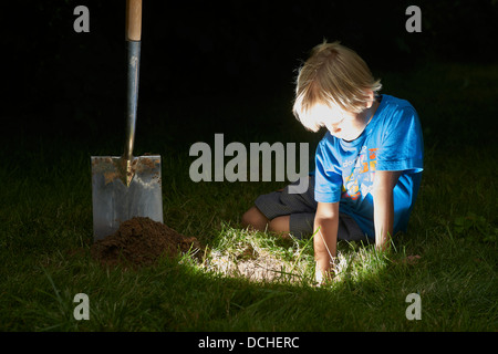 Kind junge einen Schatz in magische Loch im Boden zu graben, in der Dämmerung Stockfoto