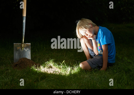 Kind junge einen Schatz in magische Loch im Boden zu graben, in der Dämmerung Stockfoto