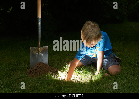 Kind junge einen Schatz in magische Loch im Boden zu graben, in der Dämmerung Stockfoto