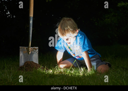 Kind junge einen Schatz in magische Loch im Boden zu graben, in der Dämmerung Stockfoto