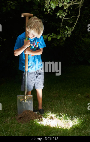 Kind junge einen Schatz in magische Loch im Boden zu graben, in der Dämmerung Stockfoto