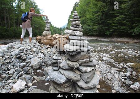 Oberstdorf, Deutschland. 18. August 2013. Eine Frau legte einen Stein auf einen Cairns auf dem trockenen Bett des Flusses Trettach in der Nähe von Oberstdorf, Deutschland, 18. August 2013. Die vom Menschen verursachten Steinhaufen sind tatsächlich als Wahrzeichen errichtet, aber sie sind auch für Spaß bei Kindern und Erwachsenen gebaut. Foto: Karl-Josef Hildenbrand/Dpa/Alamy Live News Stockfoto