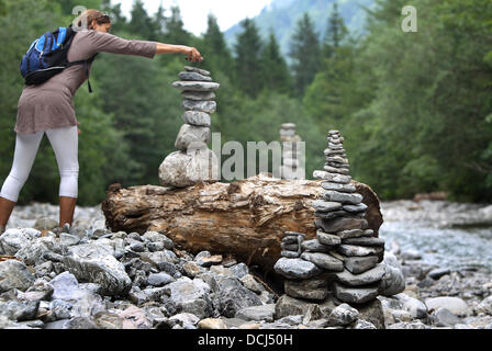 Oberstdorf, Deutschland. 18. August 2013. Eine Frau legte einen Stein auf einen Cairns auf dem trockenen Bett des Flusses Trettach in der Nähe von Oberstdorf, Deutschland, 18. August 2013. Die vom Menschen verursachten Steinhaufen sind tatsächlich als Wahrzeichen errichtet, aber sie sind auch für Spaß bei Kindern und Erwachsenen gebaut. Foto: Karl-Josef Hildenbrand/Dpa/Alamy Live News Stockfoto