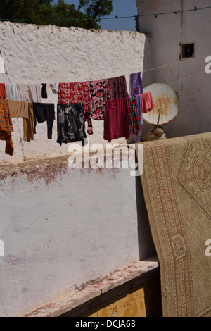 Traditionelle Teppich drapiert über eine Mauer zusammen mit Waschen Trocknen auf einer Linie.  Rostige Satellitenschüssel im Hintergrund.  Berber Dorf. Stockfoto