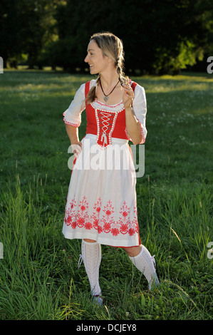 junge Frau trägt bayerische Tracht Dirndl und Zöpfe in einem park Stockfoto