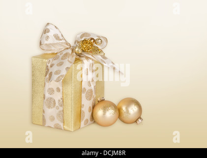 Goldenen Geschenk verpackt vorhanden mit gepunkteten Bogen und golden Christmas ball Ornamente Stockfoto