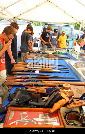 Eine Gruppe junger Männer versammeln sich, um einen Tisch draußen auf einem Flohmarkt, Blick auf Pistolen, Gewehre und andere Waffen zu verkaufen Stockfoto