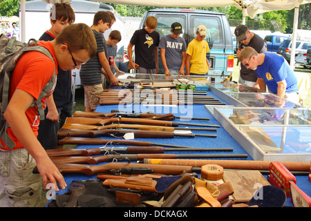 Eine Gruppe junger Männer versammeln sich, um einen Tisch draußen auf einem Flohmarkt, Blick auf Pistolen, Gewehre und andere Waffen zu verkaufen Stockfoto