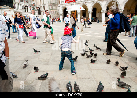 Mädchen spielen mit Tauben auf der Piazza San Marco (Markusplatz entfernt), Venedig, Italien, mit Menschen, die vorbeigehen. Stockfoto