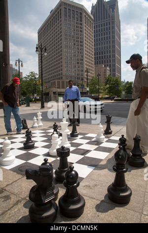 Detroit, Michigan - zwei Männer spielen Schach auf einem Bürgersteig Schachbrett in der Innenstadt von Detroit als Dritter Mann Uhren. Stockfoto