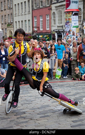 Edinburgh, Schottland, 20. August 2013, Edinburgh Fringe Festival die japanische Street Entertainerin Cheeky from 'Witty Looks' befindet sich in einer schmerzhaft aussehenden Position, als sie versucht, ihr Einrad während einer Performance auf der Royal Mile zu montieren. Stockfoto