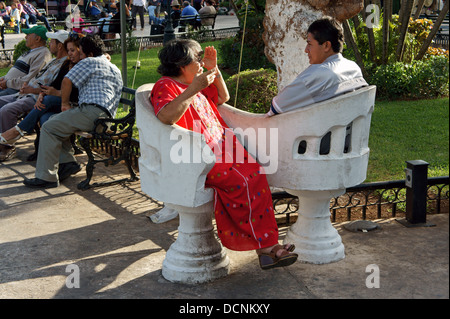 Ältere Frau und jüngerer Mann sitzen und plaudern in Liebe Sitze auf dem Hauptplatz von Merida, Yucatan, Mexiko Stockfoto