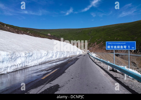 Die Autobahn in den Bergen, das Board sagen: die nächsten Kilometer kontinuierliche scharfe Wendung ", Xinjiang in China Stockfoto