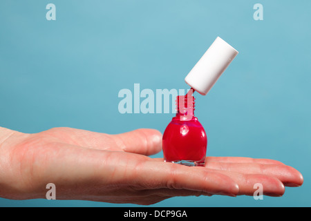 Pediküre Maniküre roten Nagellack Flasche auf weibliche Hand blauen Hintergrund Stockfoto