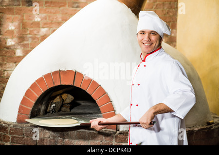 Koch legt Teig in den Ofen für Pizza, Stockfoto