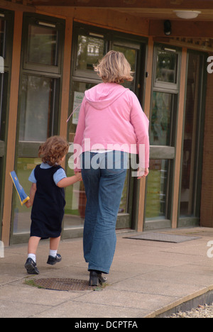 Rückansicht von Mutter und junges Mädchen in Schuluniform, die Hände haltend und zur Schule gehen