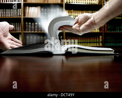 Hände halten ein altes Buch mit Bibliothek im Hintergrund Stockfoto