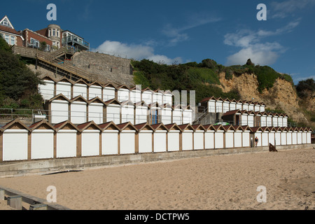 Drei Reihen von weißen doored Strandhütten in Swanage gegen die Klippen mit einer Tür, die geöffnet und blaue Vorhänge zu sehen. Stockfoto