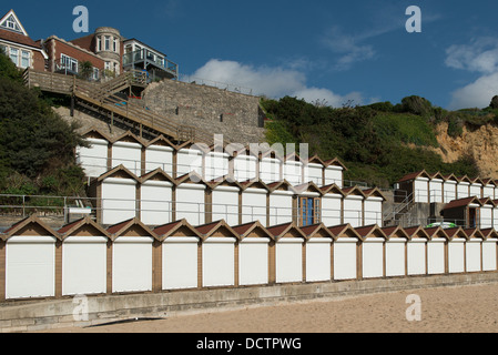 Drei Reihen von weißen doored Strandhütten in Swanage gegen die Klippen mit einer Tür, die geöffnet und blaue Vorhänge zu sehen. Stockfoto